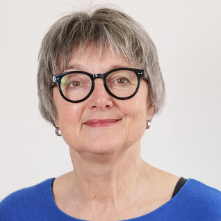 Portrait einer älteren Frau mit kurzem Haar und runder Brille.